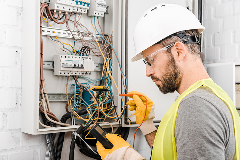 handsome electrician checking electrical box with multimetr in c